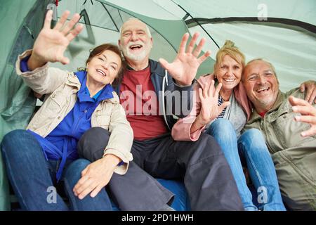 Portrait of cheerful senior couples waving while sitting in tent at forest during camping Stock Photo
