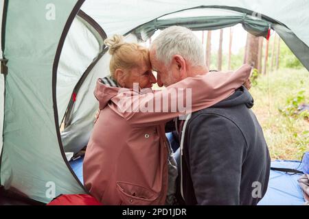 Elderly couple embracing while spending leisure time in tent during camping at forest Stock Photo