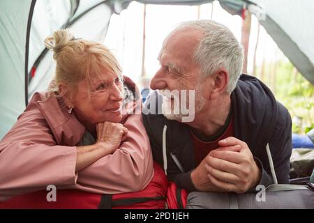 Smiling senior couple relaxing in camping tent at forest during vacation Stock Photo
