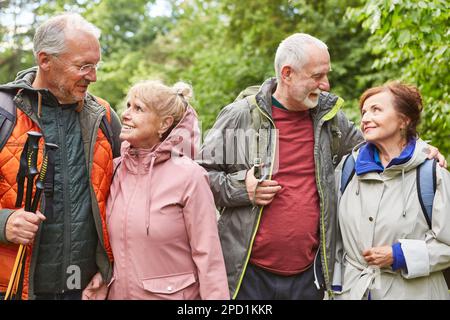 Happy elderly couples with poles and backpacks hiking together in forest during vacation Stock Photo