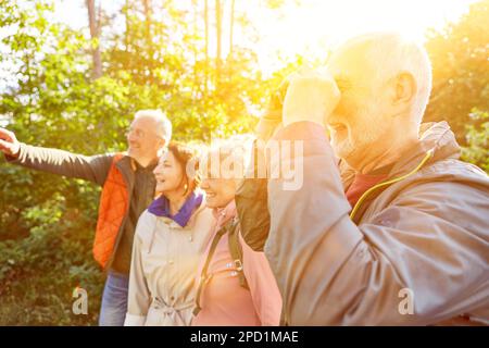 Happy elderly man bird watching through binoculars while exploring forest with friends during vacation Stock Photo