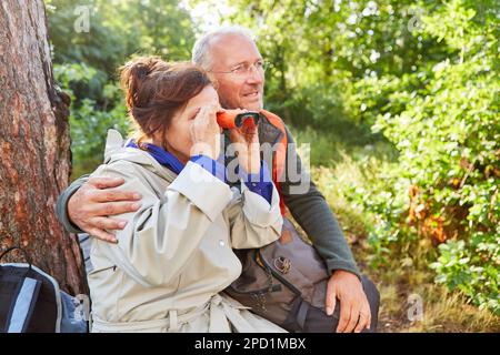 Elderly man and woman bird watching through binoculars while exploring forest in summer vacation Stock Photo