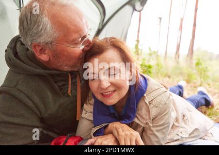 Elderly man kissing woman on head in tent during camping at forest Stock Photo