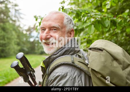Portrait of happy senior man with hiking poles and backpack during vacation Stock Photo