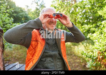 Happy senior man bird watching with binoculars in autumn forest Stock Photo