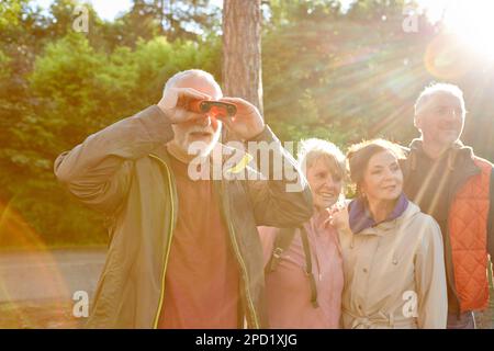 Senior man bird watching through binoculars while exploring forest with friends during vacation Stock Photo