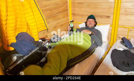 Young climber man resting inside his sleeping bag on a bunk inside a mountain refuge Stock Photo