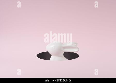 A white Easter bunny peeking out of a hole. Creative minimal concept. Stock Photo