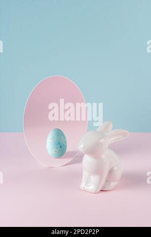 Creative concept with Easter bunny and egg in mirror on pastel pink table. Minimal Easter holiday idea. Stock Photo