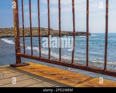 View from the pier through the rusty bridge fence over the Mediterranean sea and rocks on a sunny day in Aye Napa, Cyprus. Stock Photo