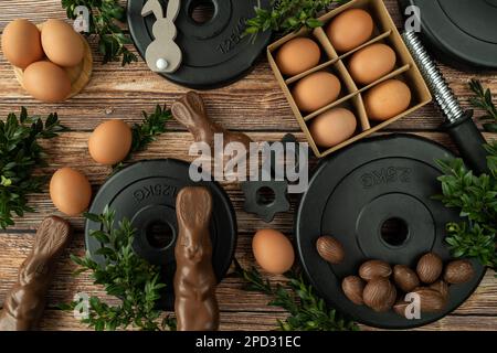 Gym dumbbells barbell weight plates, chocolate Easter bunnies, eggs and boxwood branches. Healthy diet choice concept. Fitness workout flat lay. Stock Photo