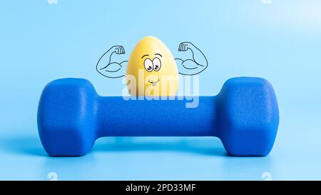 Funny Easter egg with cute face shows his muscles behind dumbbell on blue background. Strong athlete yellow egg character in theme of sports, training Stock Photo