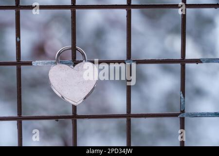 Heart shaped love padlock on a metal fence in winter with out of focus background, mock up. Stock Photo
