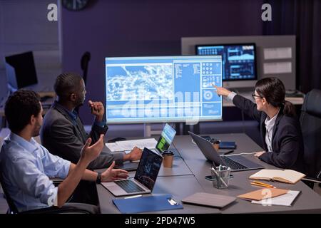 Diverse grup of business people at meeting in high tech IT office pointing at digital board with data Stock Photo