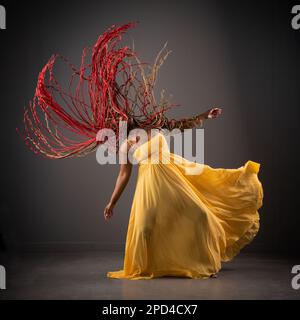 An African American female in a long, yellow dress spinning in a graceful and fluid motion Stock Photo