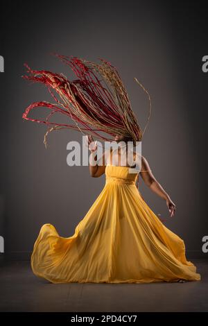 An African American female in a vibrant yellow dress dancing joyfully with moving hair Stock Photo