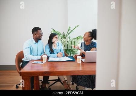 Wide shot of three business coworkers around boardroom table talking Stock Photo