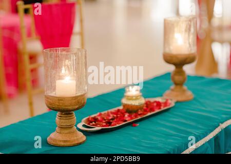 Two glass candles and vibrant flower petals on a table Stock Photo