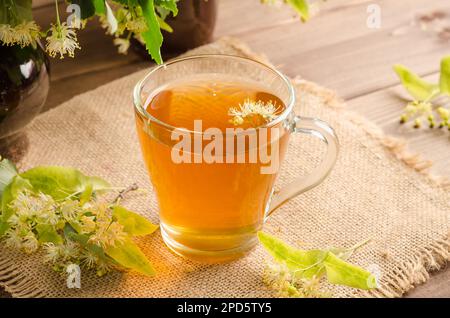 Healing herbal tea with lime blossom in a mug on a dark wooden table with flowers. Stock Photo