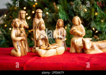 Nativity creche made of olive tree wood from the Holy Land with a Christmas tree and lights background with baby Jesus Stock Photo