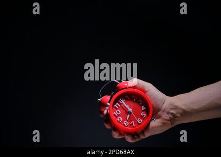 Red alarm clock showing eight in morning in hand on black background Stock Photo