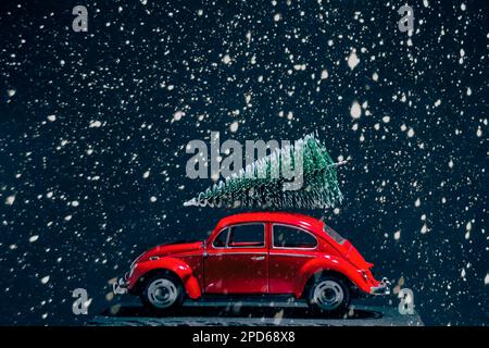 Red retro car with Christmas tree on roof during heavy snowfall Stock Photo