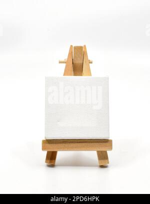 Small wooden model easel with a blank art canvas resting on it isolated on a plain white background. Copy space. No people. Stock Photo