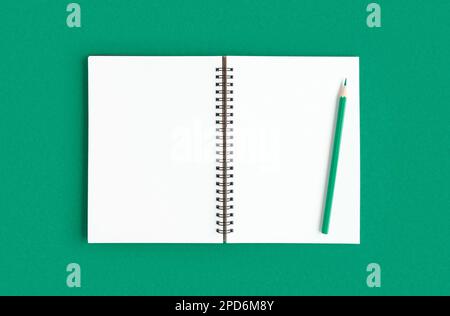 Notebook with pencil. Open notebook on green emerald color background, spiral notepad. Top view of open notepad with blank pages, office flat lay. Whi Stock Photo