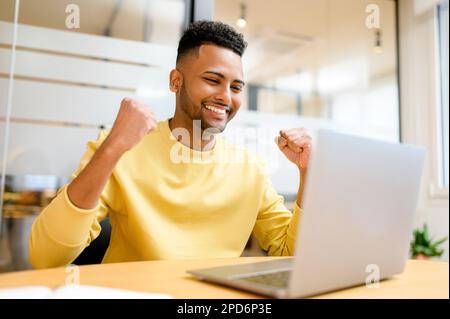Excited Pakistani businessman looking at the laptop screen and rejoicing. Happy indian guy smiling staring at display amused with unexpected opportunity, received job offer Stock Photo