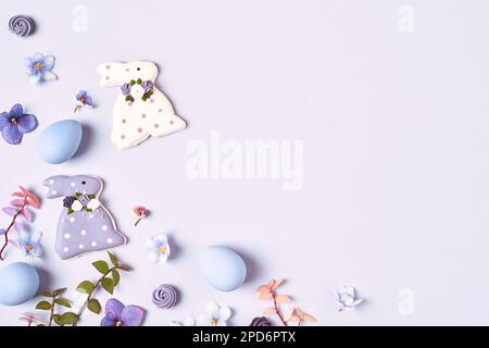 Easter background. Easter decorations, bunny, eggs and flowers on violet background. Copy space, flat lay. Corner frame. Stock Photo