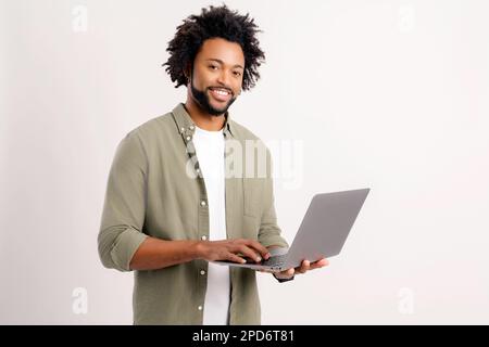 Smiling positive man holding laptop in hands and typing. Blogger making posts in social networks, chatting with followers. Indoor studio shot isolated on white background Stock Photo