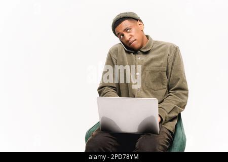 Busy young african-american man sitting with laptop computer and talking by smartphone, concentrated guy having important phone conversation isolated over white background Stock Photo