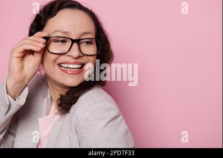 Happy middle-aged pretty woman, teacher in classic light gray suit ans stylish glasses, smiling broadly on pink background Stock Photo