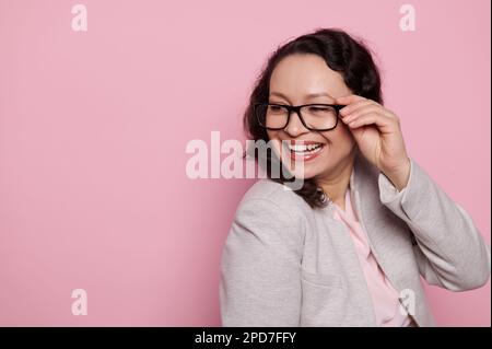 Beautiful woman in stylish eyeglasses, smiling broadly looking aside, isolated on pink background with free ad space Stock Photo