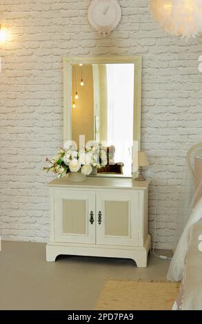 White elegant bedside table with square mirror located in bedroom as interior cosy room Stock Photo