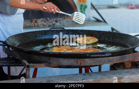 Cook female roasts flour pastries in a large pan with butter outdoor Stock Photo