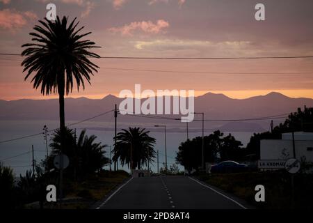 view towards fuertaventura at sunset along a road leading down to la asomada tias Lanzarote, Canary Islands, Spain Stock Photo
