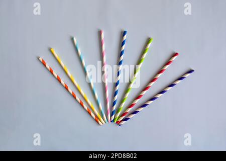 Disposable colorful striped paper cocktail sticks for party on blue background. Eco friendly paper drinking straws. Stock Photo