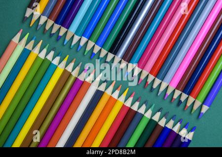 Color pencils on green background. Arrangement of multicolored pencils. Top view. Close-up. Selective focus. Stock Photo