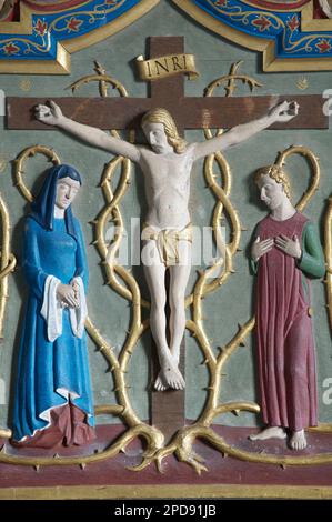 Carved and painted depiction of the crucifixion of Jesus Christ on a reredos behind the altar of St Laurence’s Church, Affpuddle, Dorset, England, UK. Stock Photo