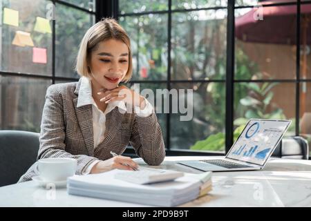 Young business woman checking paperwork from accounting department to analyse number on document, using computer laptop to check database Stock Photo