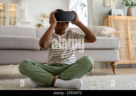 African American boy child sitting on floor at home using virtual reality device watching 3d video Stock Photo
