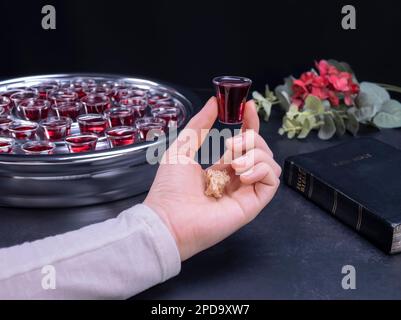 Closeup of young woman taking communion the wine symbol of Jesus Christ blood in small cups on black background. Easter Passover and Lord Supper conce Stock Photo