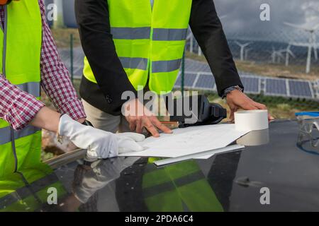 Close-up of the hands of two engineers analyzing a technical drawing at a solar power plant. Stock Photo