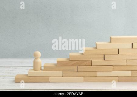 wooden figurine of a man stands on a staircase made of blocks on the first step. The concept of achieving the set goals in business, career growth, st Stock Photo