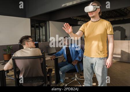 IT Development Team Working on VR Project. Man wearing VR headset, playing and touching something in the virtual world. Diverse men programmers using Stock Photo