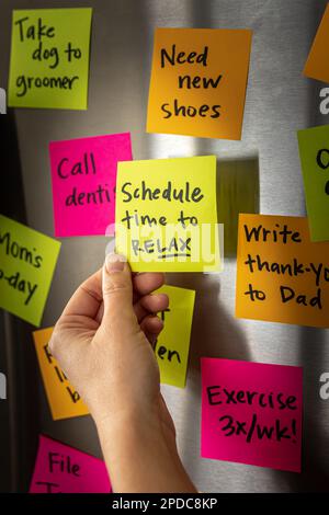 Hand Holding Schedule Time to Relax Sticky Note Memo to Fridge Door Full of Colorful Reminders Stock Photo
