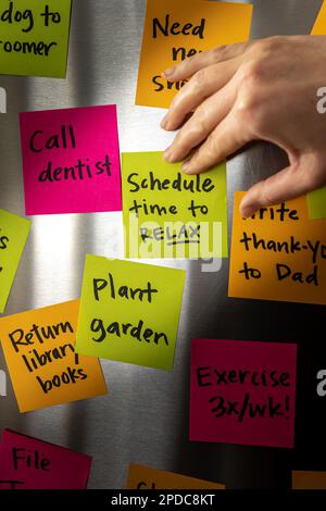 Hand Holding Schedule Time to Relax Sticky Note Memo to Fridge Door Full of Colorful Reminders Stock Photo