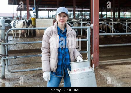 Milkmaid with aluminium cans near open cowshed at dairy farm Stock Photo