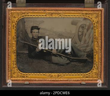 Unidentified soldier in Union uniform lying on grass, with musket, in front of painted backdrop showing cannon, American flag, and landscape. Liljenquist Family Collection of Civil War Photographs , FAmbrotype/Tintype photograph filing series , pp/liljunion. United States, Army, People, 1860-1870, Soldiers, Union, 1860-1870, Military uniforms, Union, 1860-1870, Rifles, 1860-1870, Backdrops, 1860-1870, United States, History, Civil War, 1861-1865, Military personnel, Union. Stock Photo